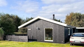Un bâtiment moderne à l’extérieur sombre, avec une cheminée bien visible et une voiture garée devant.