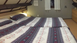 A bedroom with a sloped ceiling, a bed with patterned bedding, a nightstand, a dresser, and a window with curtains. - Fischerhaus by the sea (Bredene)