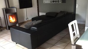 A living room with a black sofa, a fireplace, a TV mounted on the wall, and a tiled floor. - Fischerhaus by the sea (Bredene)