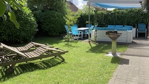 A patio area with a wooden lounge chair, a white outdoor sofa, and a table with chairs. - Fischerhaus by the sea (Bredene)