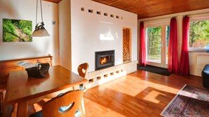 A cozy living room with a fireplace, wooden flooring, and a dining area with a table and chairs. - Holiday Home Black Forest (Feldberg)