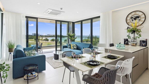 A modern living room with a large window, a dining area, and a kitchen.