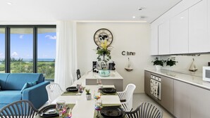 A modern dining area with a view of the ocean, a blue sofa, and a kitchen with white cabinets.