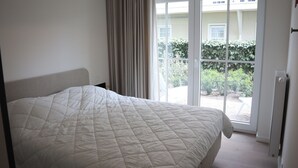 A bedroom with a large bed, a window with curtains, and a view of greenery outside.