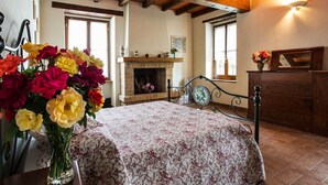 A room with a bed, a fireplace, a wooden dresser, and a vase of flowers. - Sunny Holiday Home With Swimming Pool (Salsomaggiore Terme)