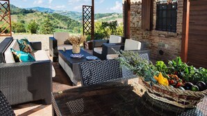 An outdoor seating area with wicker furniture, a table with plates, and a basket of fruits. - Sunny Holiday Home With Swimming Pool (Salsomaggiore Terme)