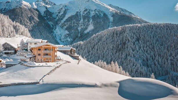 A snow-covered mountain landscape with a wooden chalet-style building featuring multiple balconies and a snow-covered driveway.