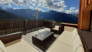 A terrace with outdoor furniture, a wooden fence, and a view of mountains.