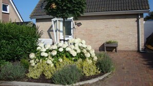 Une maison avec un toit en tuiles, une façade en briques et un jardin agrémenté de fleurs blanches et d’arbustes.