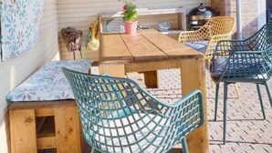 Un patio couvert avec une table et des chaises en bois, un banc et une plante suspendue.