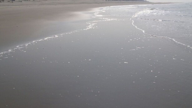 Une plage avec un phare qui se dessine à l'horizon.