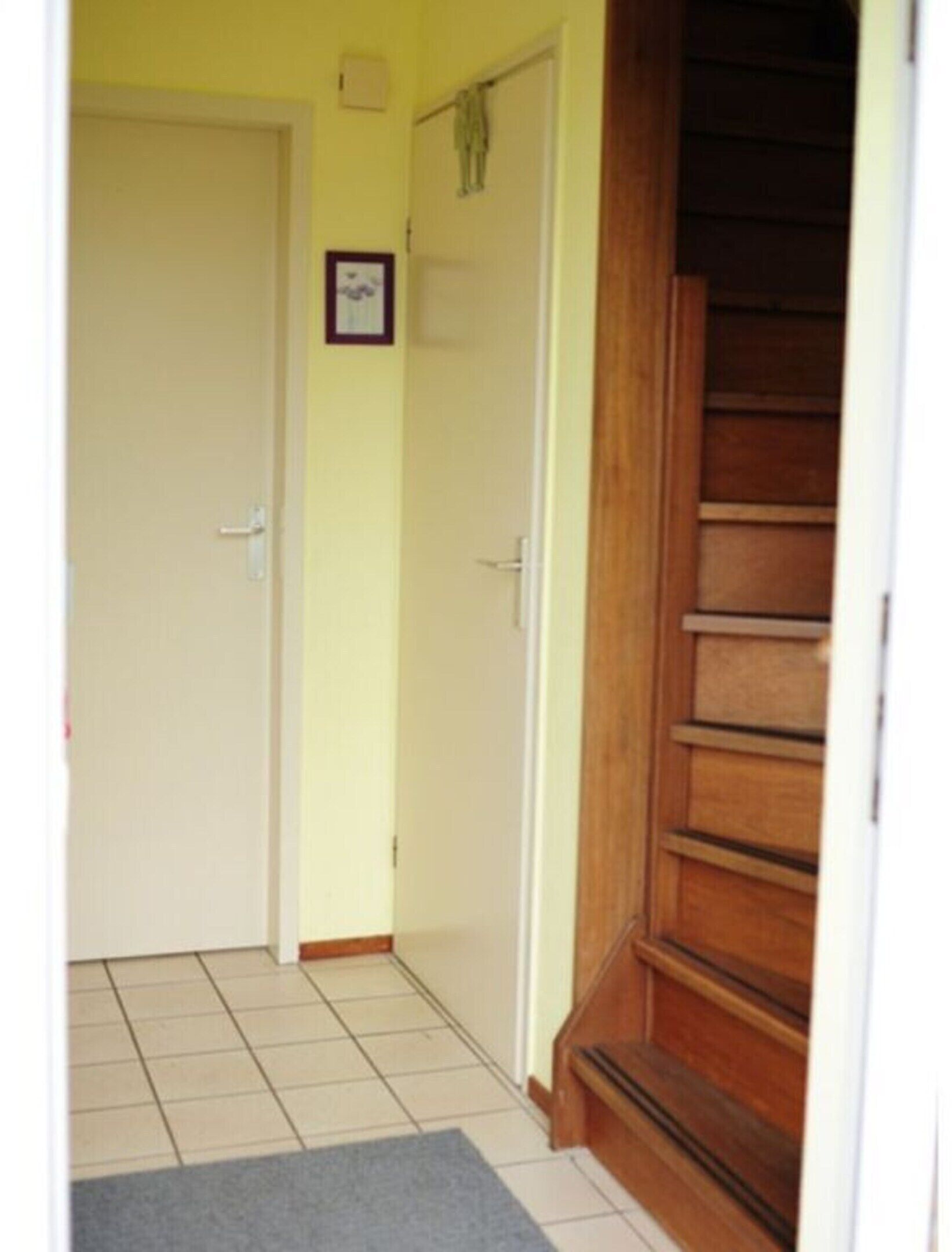 A hallway with a wooden staircase, a tiled floor, and a door with a picture frame on the wall.