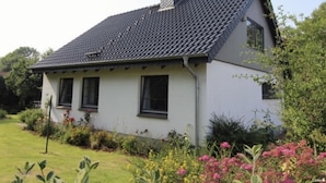 A single-story house with a dark tiled roof, white exterior walls, and a small garden with various plants and flowers. - Holiday Home Backbert Near Kappeln (Kappeln)