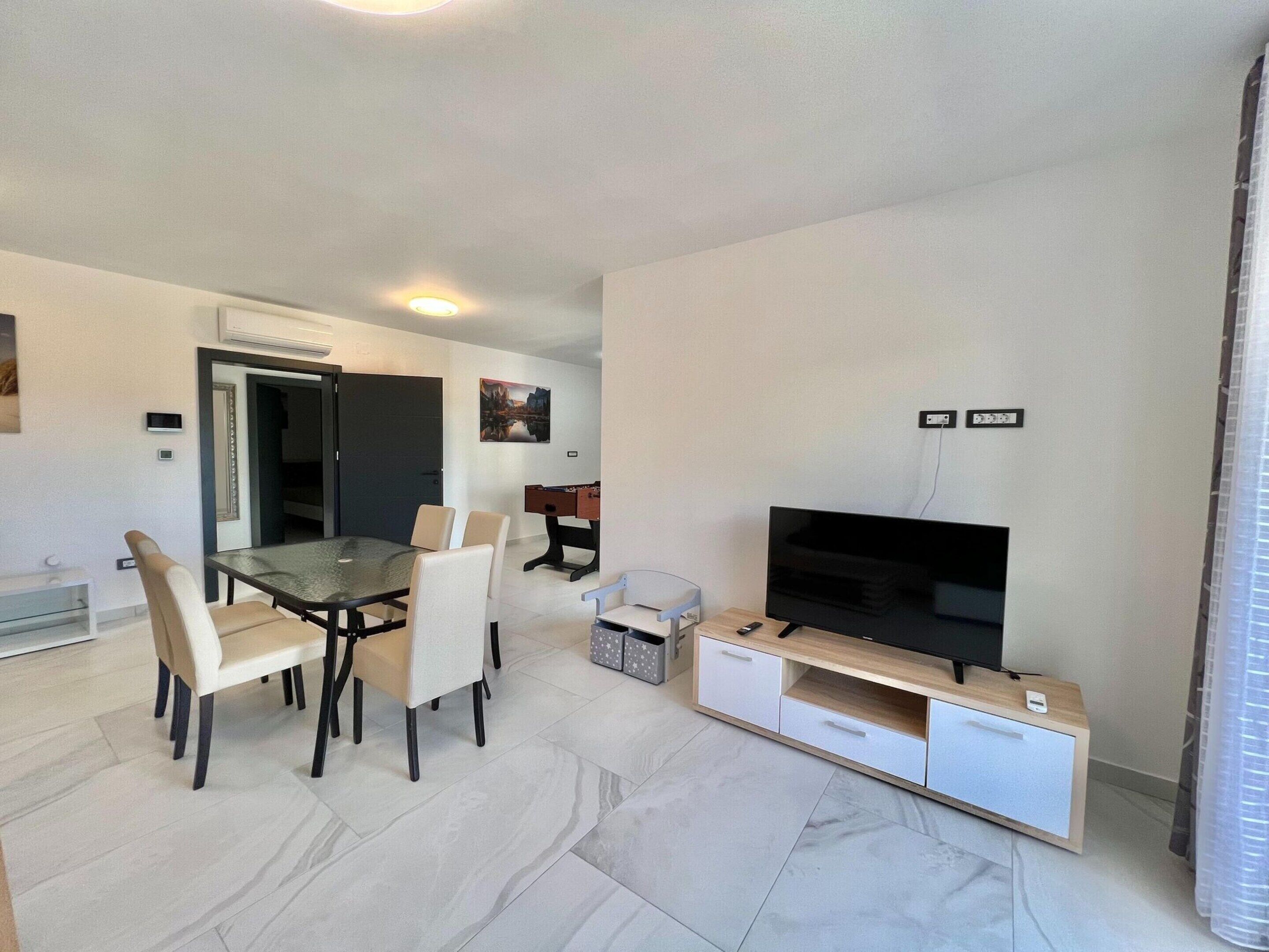 A modern living room with a dining area, a flat-screen TV, and a foosball table.
