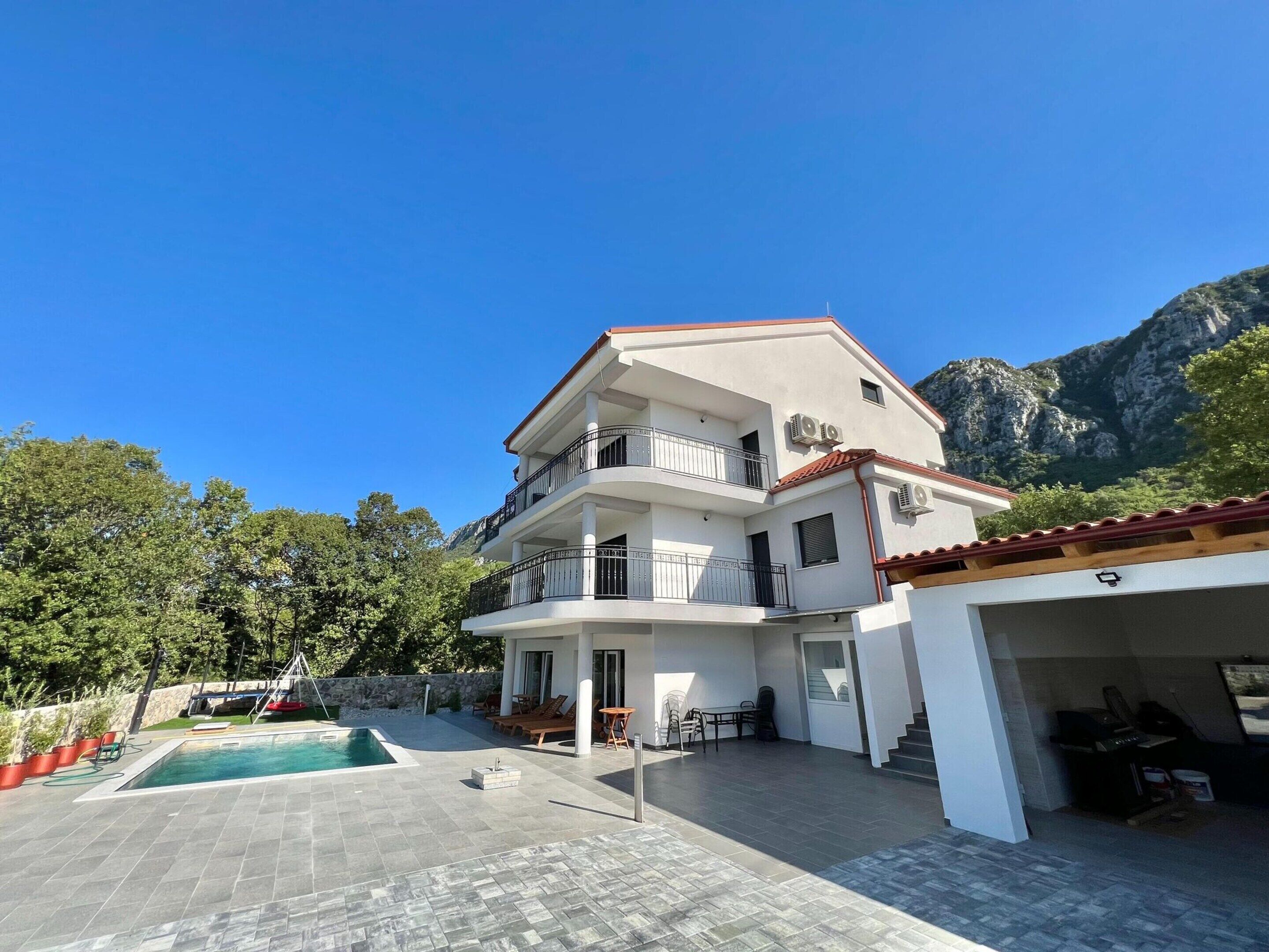 A multi-story building with a swimming pool, outdoor seating, and a garage.