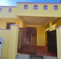 Um edifício amarelo com portão, um pequeno alpendre e um caminho de tijolos até a porta.