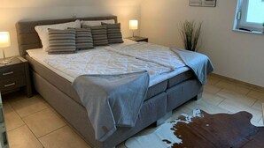 Een slaapkamer met een bed, nachtkastjes, een lamp, een raam en een vachttapijt van koeienhuid.