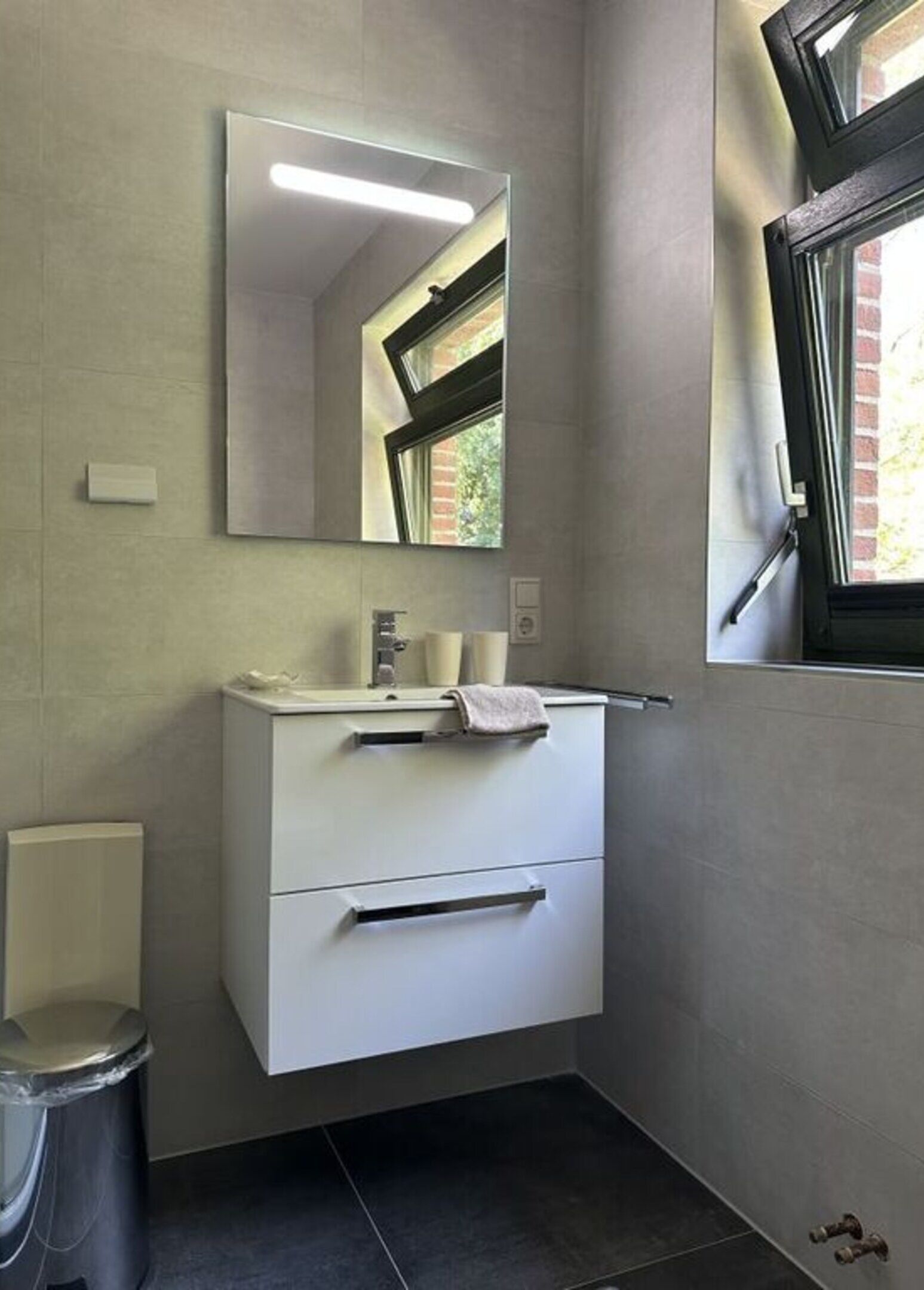 Un baño moderno con tocador blanco, espejo y ventana.