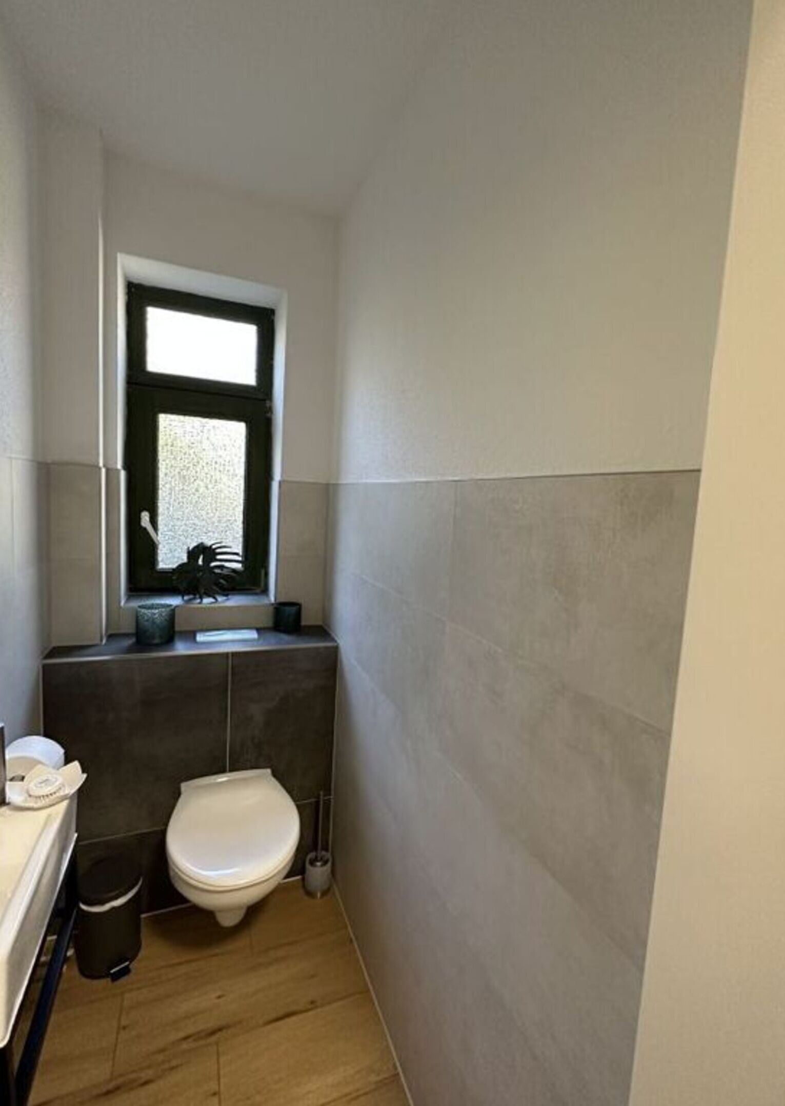 A compact bathroom with a toilet, a small window, and a mirror above the sink.