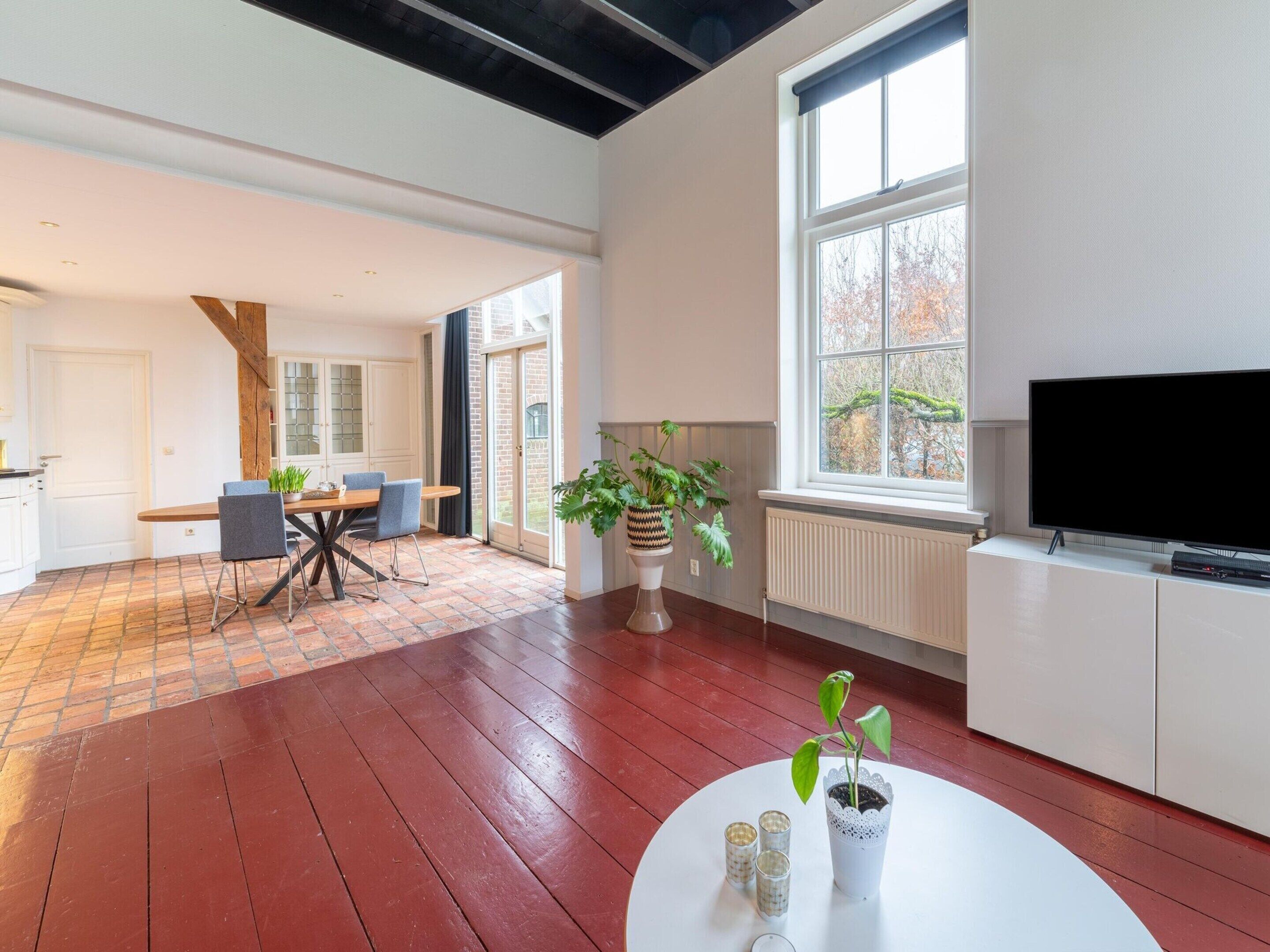 A spacious living area with a large window, a flat-screen TV, and a dining table with chairs.