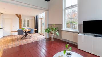 A spacious living area with a large window, a flat-screen TV, and a dining table with chairs.