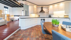 A modern kitchen with white cabinets, a central island, and a dining area with blue chairs. - Comfortable Farmhouse With Terrace (Nijeveen)