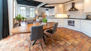 A modern kitchen with white cabinets, a black range hood, and a dining area with a wooden table and chairs. - Comfortable Farmhouse With Terrace (Nijeveen)