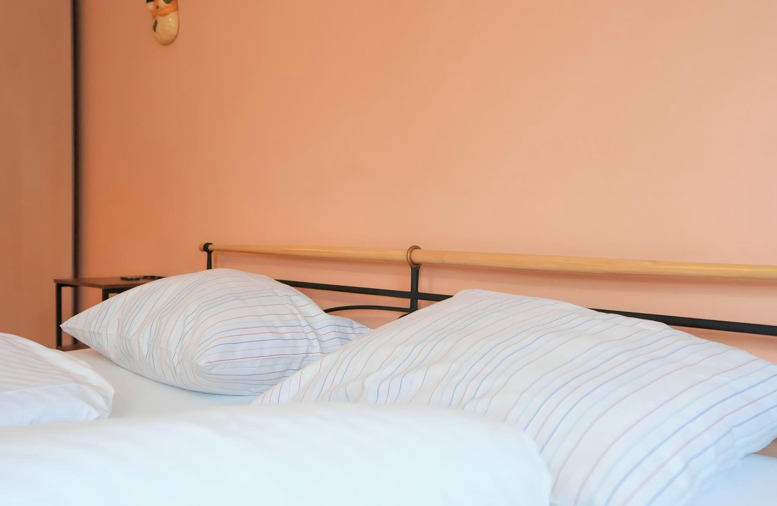 A bed with striped bedding and a wooden headboard in a room with peach-colored walls.