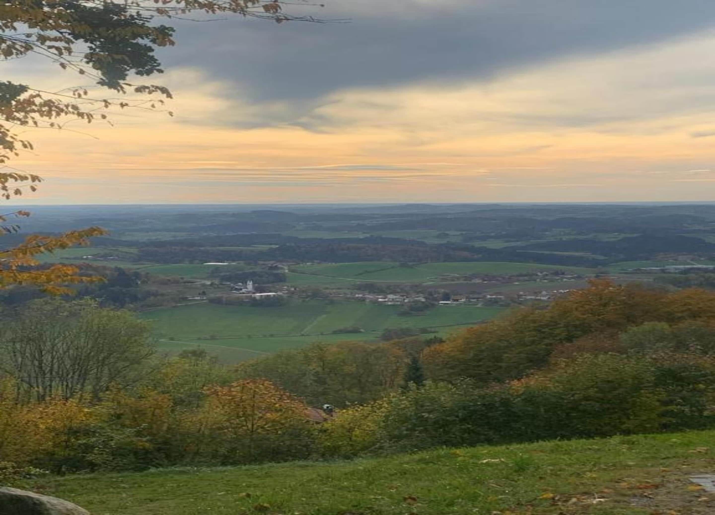 A panoramic view of a rural landscape with rolling hills, a small village, and a church.