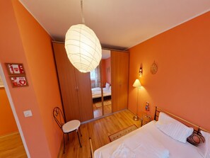A bedroom with a bed, a chair, a bedside lamp, a wardrobe, and a mirror. - Appartement Sandra im Bayerischen Wald mit Pool (Freyung)