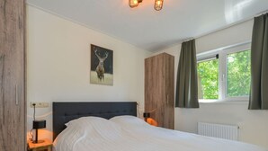 A bedroom with a large bed, a nightstand with a lamp, a wooden wardrobe, a painting of a deer, and a window with curtains. - Pavilion 6 People With Storage Space (Zorgvlied)
