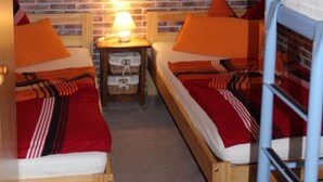 Una habitación con dos camas de madera, una pared de ladrillo y una mesita con lámpara.