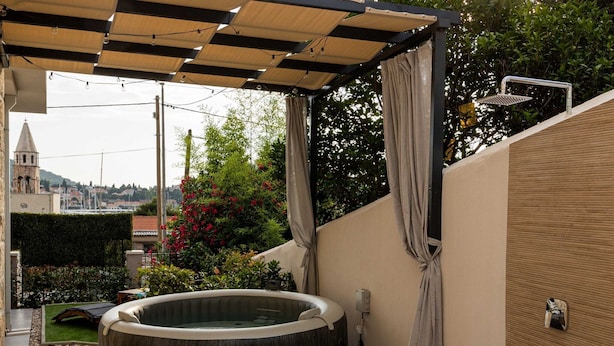 A hot tub in a covered outdoor area with a pergola overhead, a showerhead, and a view of a town in the background. - Apartments Amare - Three Bedroom Apartment With Terrace and Jacuzzi (Dubrovnik)