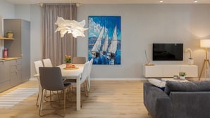 A modern living room with a dining area, a painting of sailboats, a flat-screen TV, and a grey sofa. - Apartments Amare - Three Bedroom Apartment With Terrace and Jacuzzi (Dubrovnik)