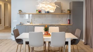 A modern kitchen with a white dining table, grey chairs, and a unique light fixture. - Apartments Amare - Three Bedroom Apartment With Terrace and Jacuzzi (Dubrovnik)
