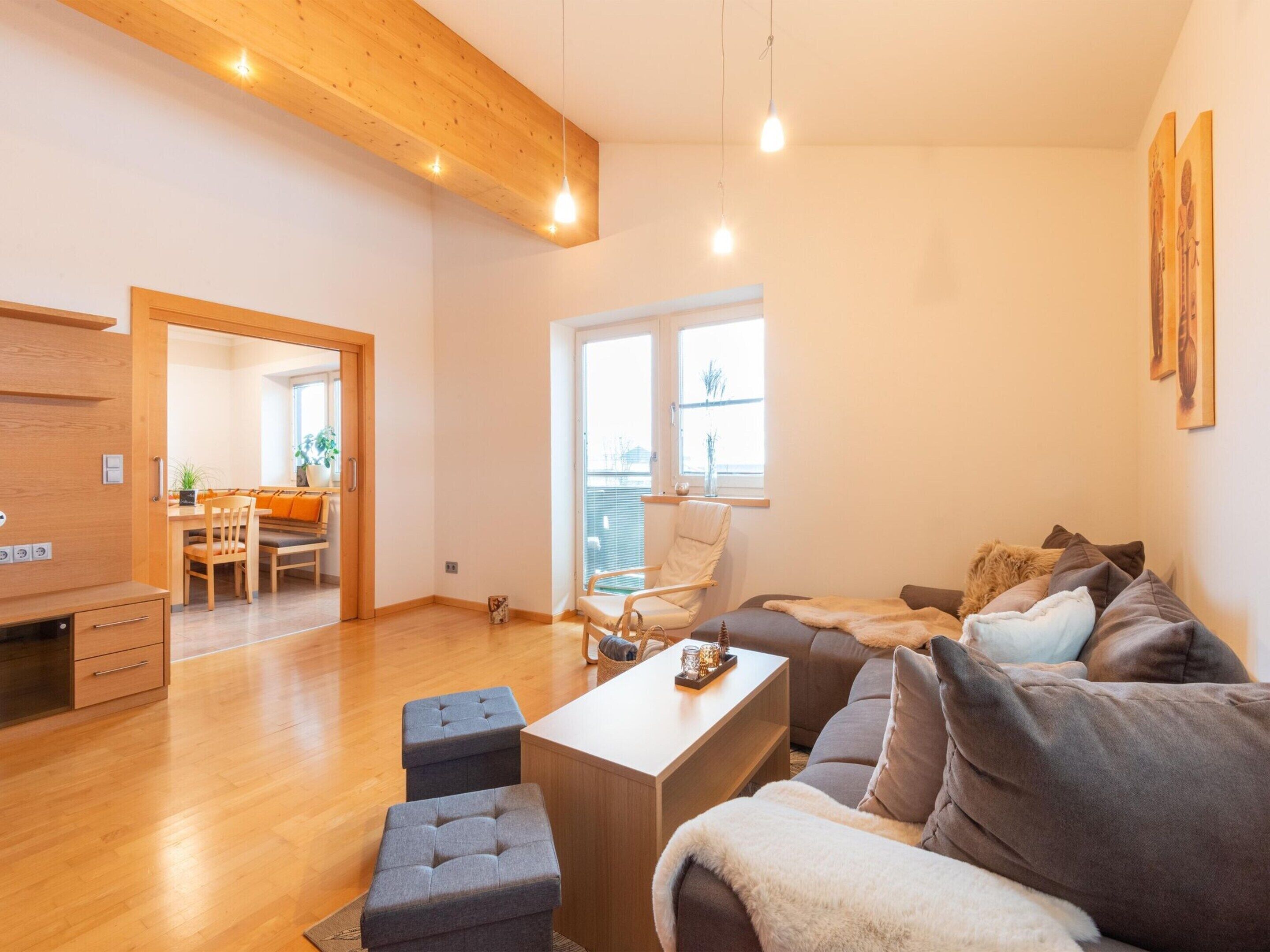 A modern living room with a wooden ceiling, a sofa set, a coffee table, and a dining area visible through an open door.