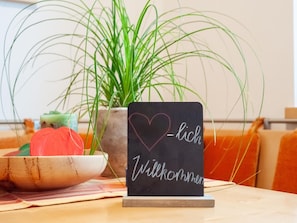 A blackboard with a heart and the words "Willkommen" and "lich" on it, placed on a table with a bowl of fruit and a plant in the background. - Apartment in Niedernsill Near Ski Slopes (Niedernsill)