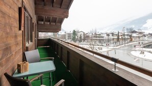 A balcony with a table and chairs, overlooking a snowy town with buildings and a bridge. - Apartment in Niedernsill Near Ski Slopes (Niedernsill)