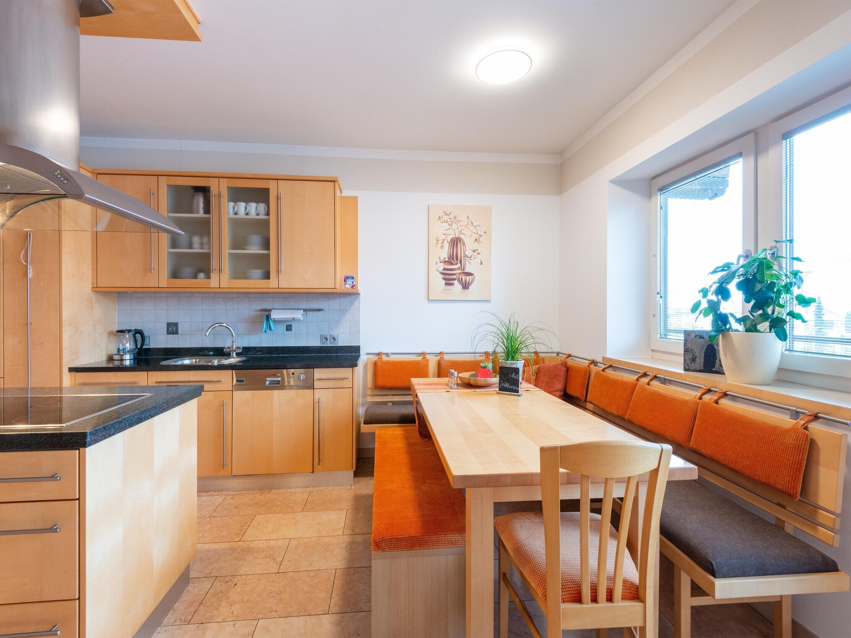 A modern kitchen with wooden cabinets, a black countertop, and a dining area with a bench and chairs.