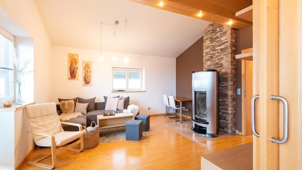 A modern living room with a sofa, coffee table, and a fireplace. There is a dining area with a table and chairs, and a kitchen area with a refrigerator. - Apartment in Niedernsill Near Ski Slopes (Niedernsill)