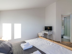 Una habitación de hotel moderna con una cama, un escritorio pequeño con televisor y una zona de ducha.
