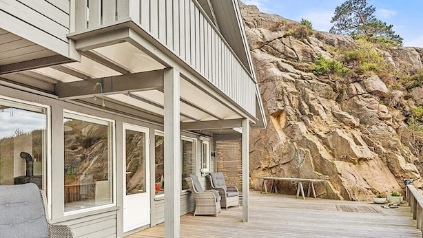 A wooden deck with outdoor furniture, a rock wall, and a clear view of the surrounding landscape. - 10 Person Holiday Home in Lindesnes (Lindesnes)