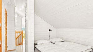 A bedroom with a sloped ceiling, a bed with white bedding, a bedside lamp, and a wooden staircase. - 10 Person Holiday Home in Lindesnes (Lindesnes)