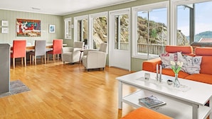 A spacious living area with a wooden floor, a dining set, and a sofa with cushions. Large windows offer a view of the outdoors. - 10 Person Holiday Home in Lindesnes (Lindesnes)
