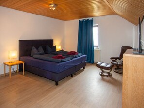 A bedroom with a wooden ceiling, a bed with pillows, a nightstand with a lamp, a chair, and a desk. - am Wehr Comfortable Holiday Residence (Allersberg)