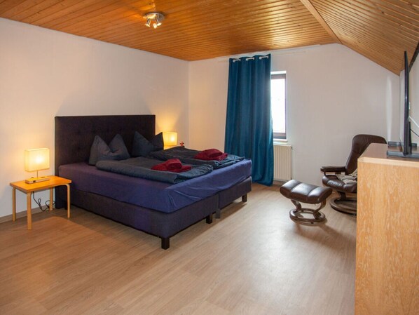 A bedroom with a wooden ceiling, a bed with pillows, a nightstand with a lamp, a chair, and a desk. - am Wehr Comfortable Holiday Residence (Allersberg)