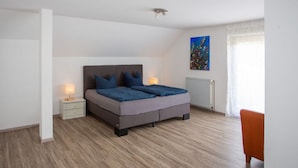 A bedroom with a bed, nightstands, a radiator, a painting, and a window with curtains.
