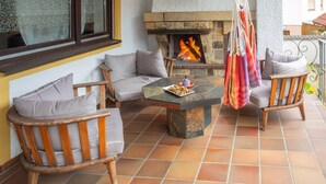 A patio with a stone fireplace, cushioned seating, and a hanging macrame chair.