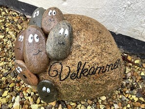 Una roccia con un volto e la scritta 'Welcome' intagliata, circondata da altre rocce decorate in modo simile.