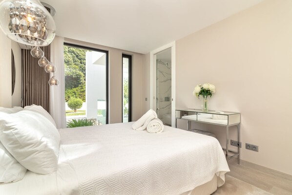Un dormitorio moderno con una cama grande, un escritorio de vidrio y vistas a zonas verdes.